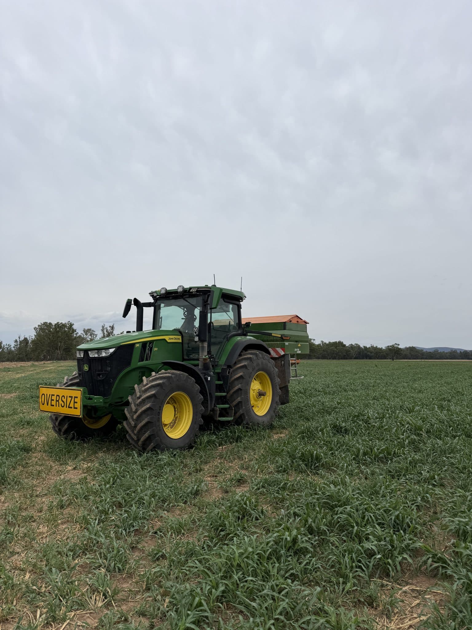 Green tractor with large yellow wheels sits in a grassy field, front sign reads 'OVERSIZE'.