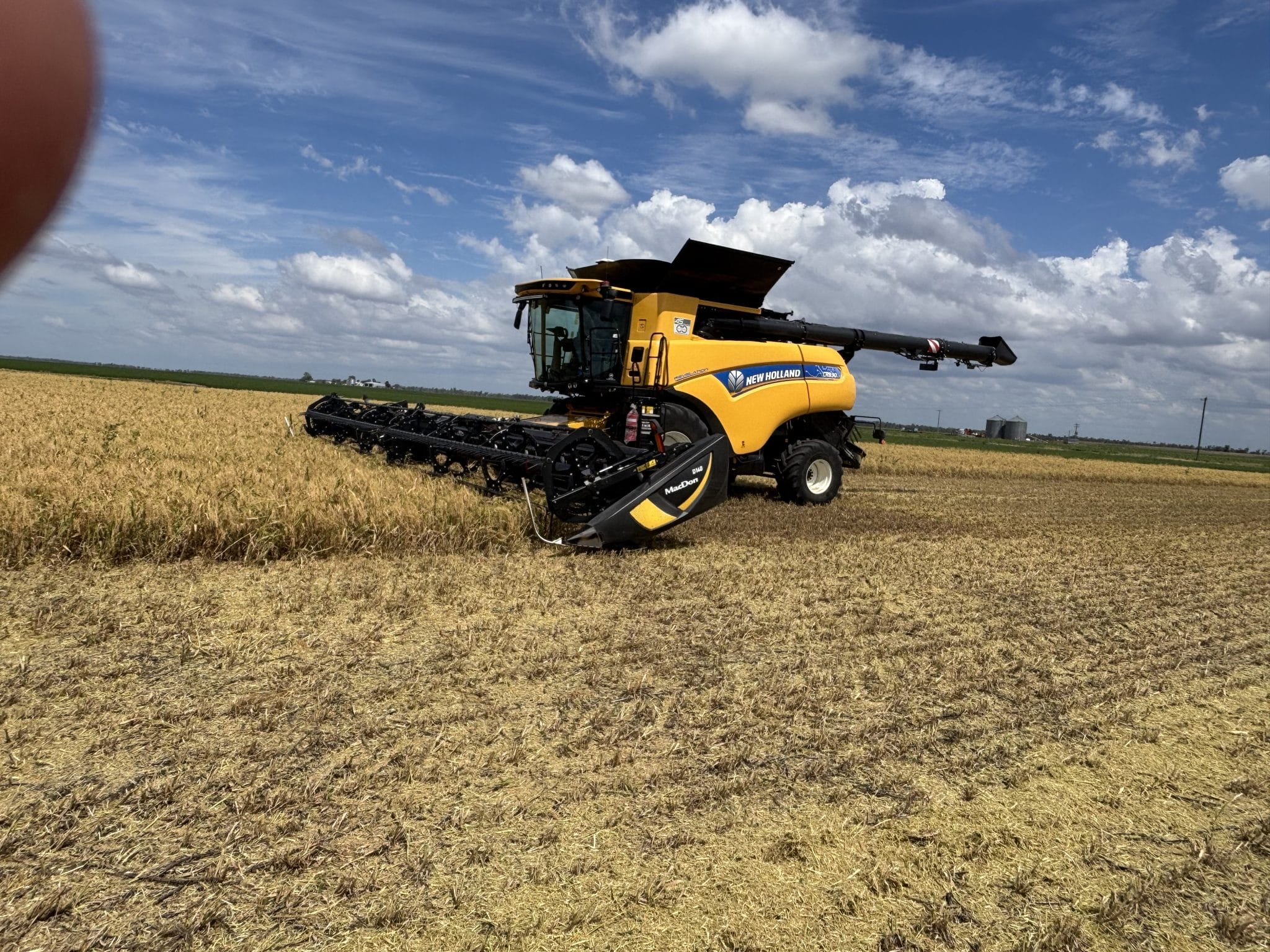 Yellow New Holland combine harvester in a harvested field under a blue sky with scattered clouds.